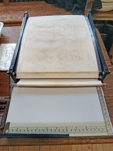 Eine geöffnete Druckpresse mit leeren Blättern und einem Maßband darunter.