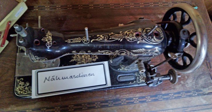 Antike Nähmaschine mit verziertem Gehäuse und großer Handkurbel.